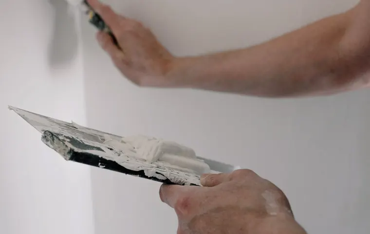 Hands applying compound to a wall during drywall repair